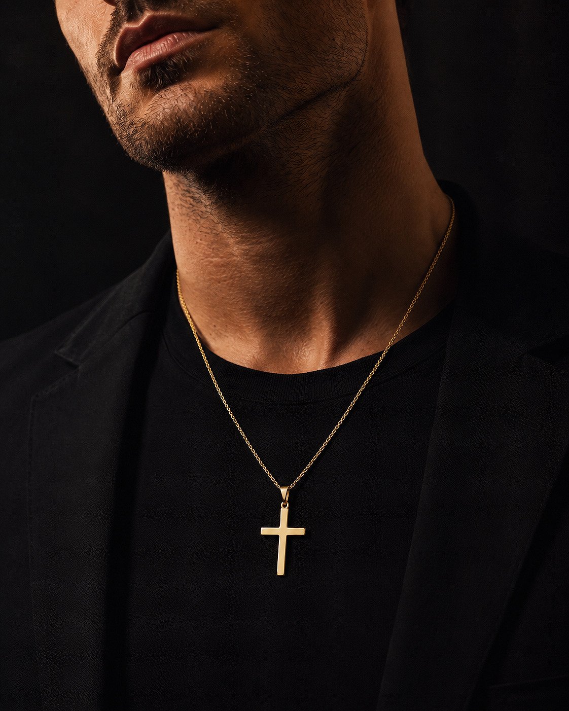 Close-up of a polished 14K yellow gold cross necklace on an adult male model.