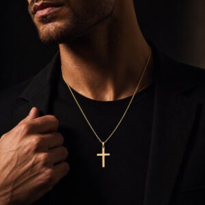 Adult male model wearing a 14K yellow gold cross necklace in a dark luxury studio setting.