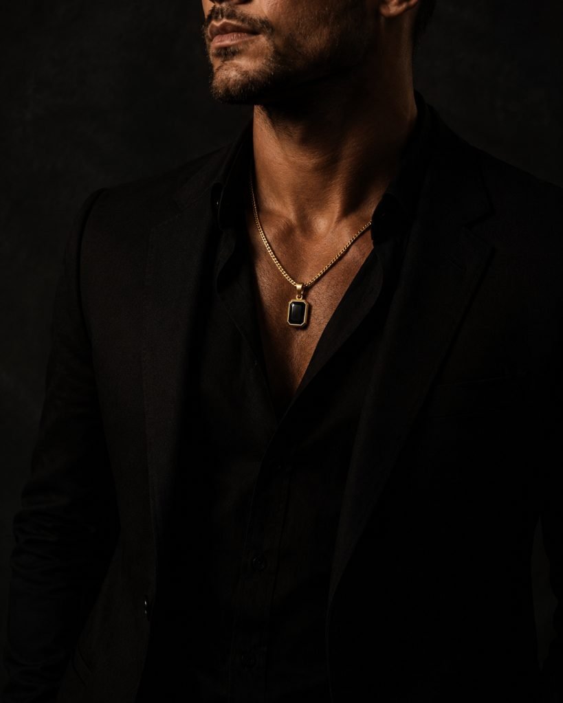 Man in a black suit wearing a gold chain with a bezel-set black stone pendant — Midori Diamond metal and stone, chosen per piece